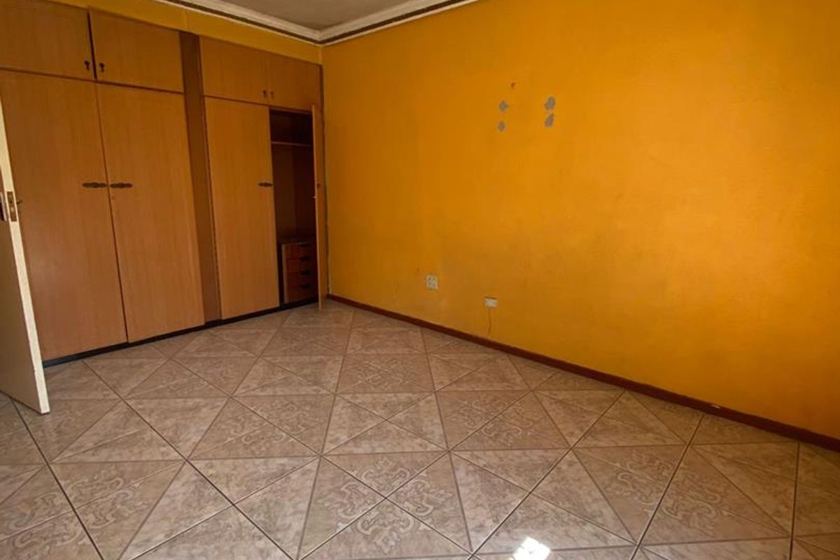 An empty bedroom featuring built-in wooden cupboards, tiled flooring, and a central ceiling light fixture.