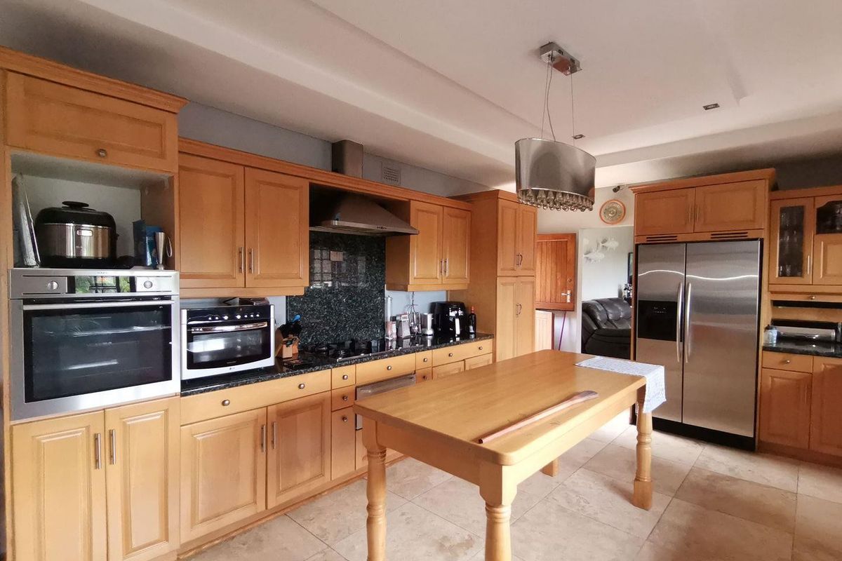 A spacious kitchen featuring light wood cabinetry, granite countertops, a central island, and integrated stainless steel appliances.