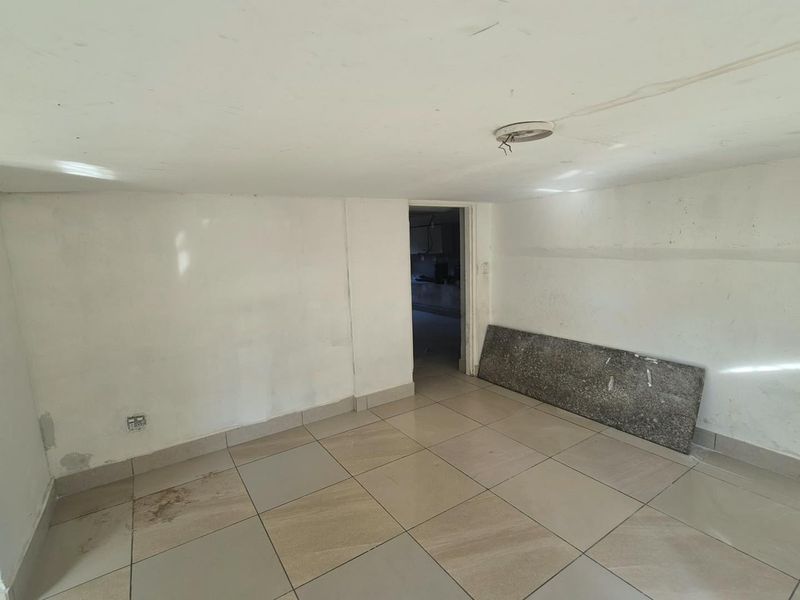 An empty, unfinished room featuring tiled flooring, exposed electrical wiring, and plain walls, offering a blank canvas for renovation or interior design projects.