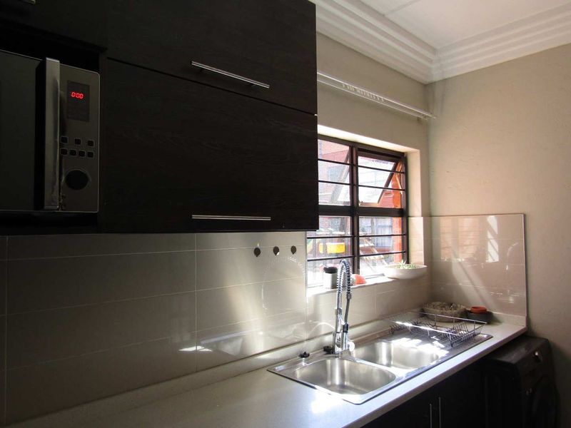 A functional kitchen featuring dark wood cabinetry, stone countertops, a double basin sink, and a built-in microwave with a tiled splashback.