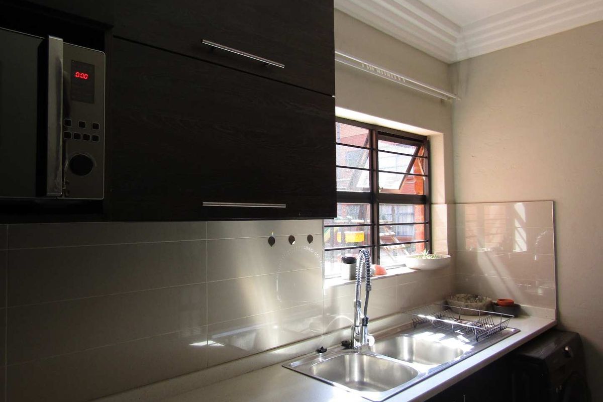 A functional kitchen featuring dark wood cabinetry, stone countertops, a double basin sink, and a built-in microwave with a tiled splashback.