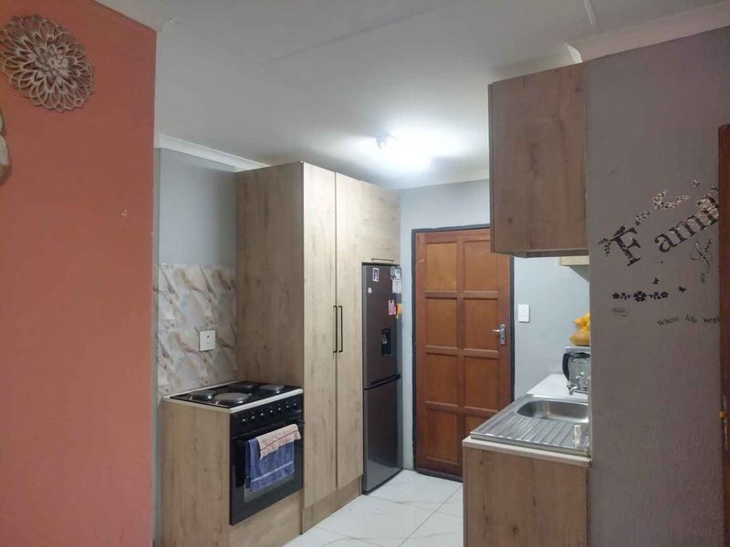Compact kitchen featuring wood-look cabinetry, tiled splashbacks, a stainless steel sink, and a freestanding stove with oven.