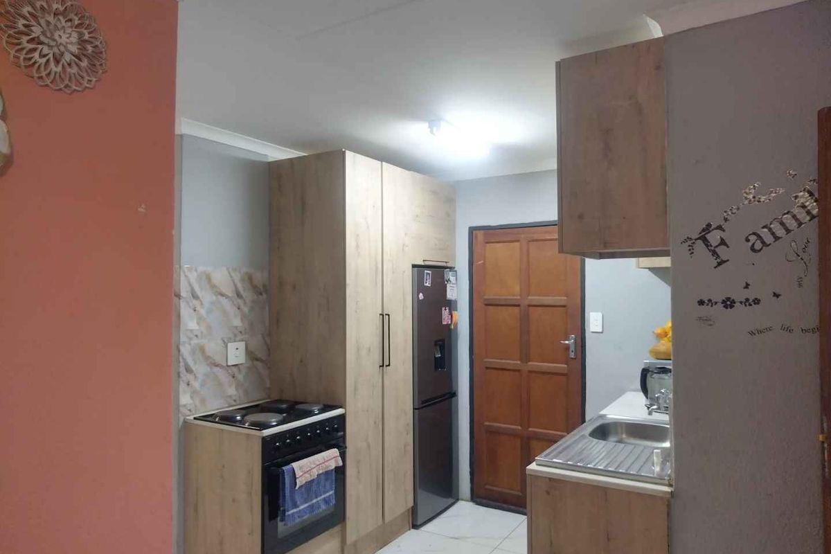 Compact kitchen featuring wood-look cabinetry, tiled splashbacks, a stainless steel sink, and a freestanding stove with oven.