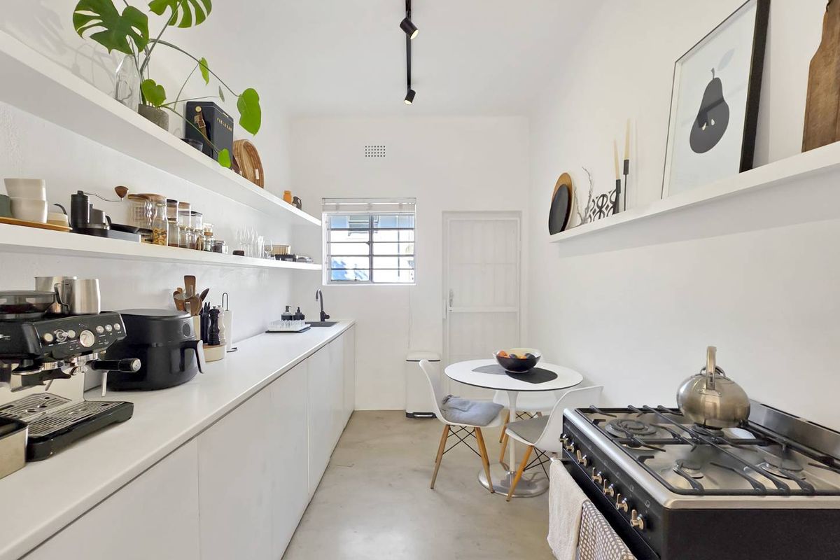 A modern, minimalist kitchen featuring sleek white cabinetry, open shelving, a gas stove, and polished concrete flooring, creating a clean and functional culinary space.