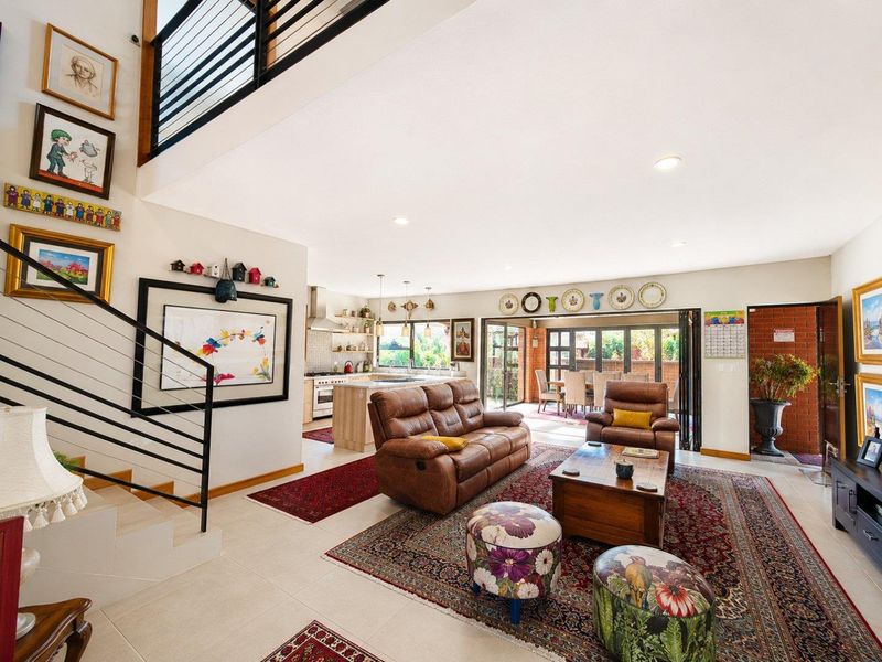 Spacious open-plan living area featuring a modern kitchen, staircase with metal balustrade, and bi-fold doors leading to an outdoor patio area.