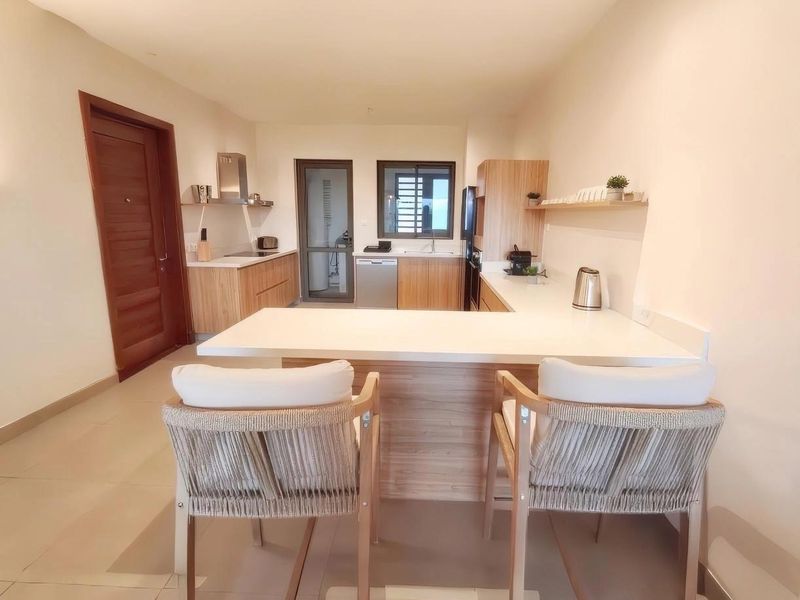 Modern kitchen featuring light wood cabinetry, stone countertops, a functional breakfast bar, and integrated appliances, creating a clean and efficient culinary space.