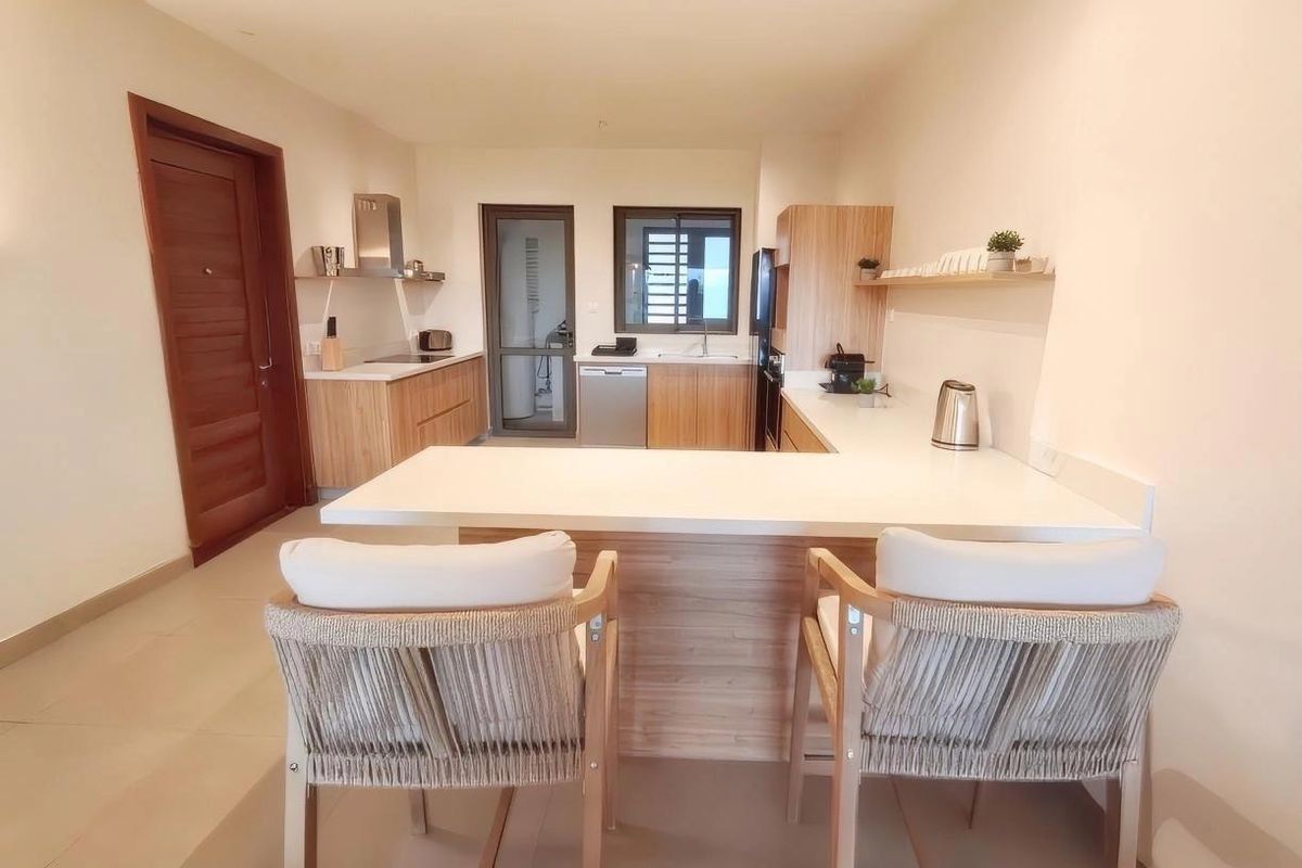 Modern kitchen featuring light wood cabinetry, stone countertops, a functional breakfast bar, and integrated appliances, creating a clean and efficient culinary space.