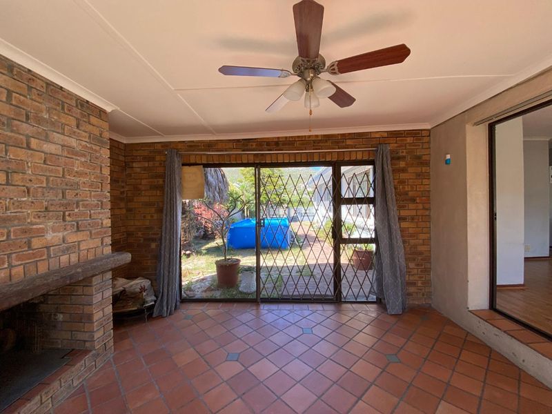 Covered patio area featuring a brick fireplace, ceiling fan, and tiled flooring, with direct access to the rear garden through a sliding security door.