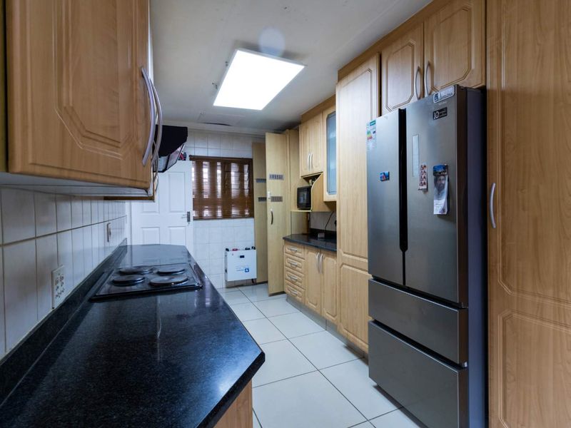 A functional kitchen featuring light wood cabinetry, dark granite countertops, an electric hob, and tiled flooring with ample storage space.