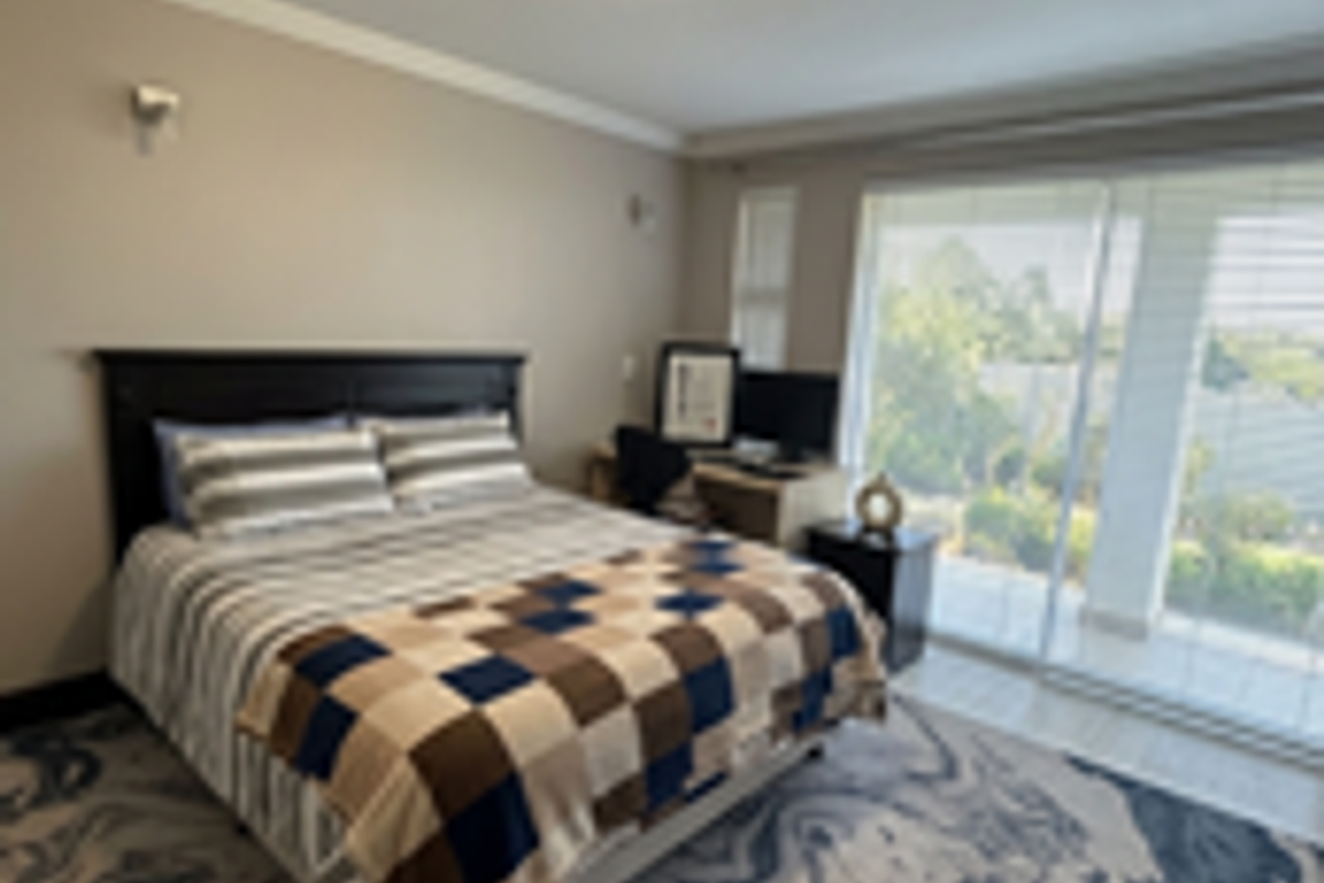 A well-maintained bedroom featuring a sliding glass door providing natural light and access to an outdoor area, complemented by modern ceiling and wall lighting.