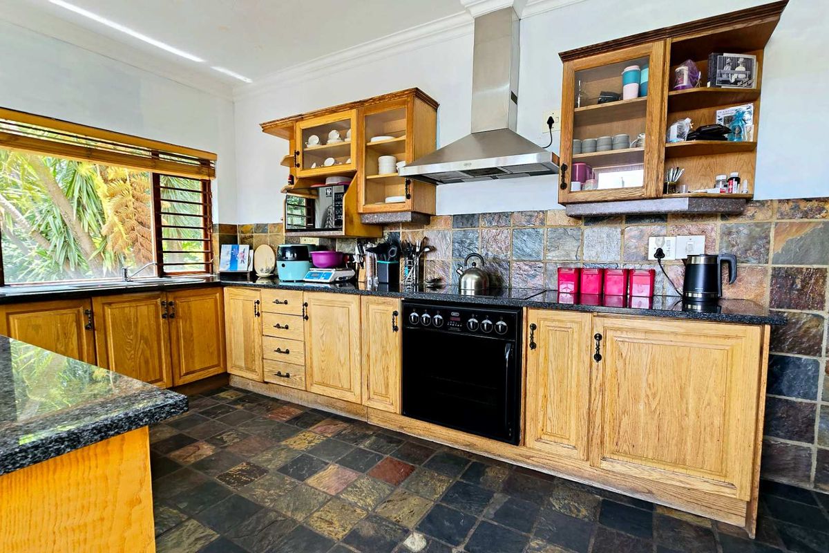 A functional kitchen featuring solid wood cabinetry, granite countertops, a stainless steel extractor fan, and natural slate tile flooring.