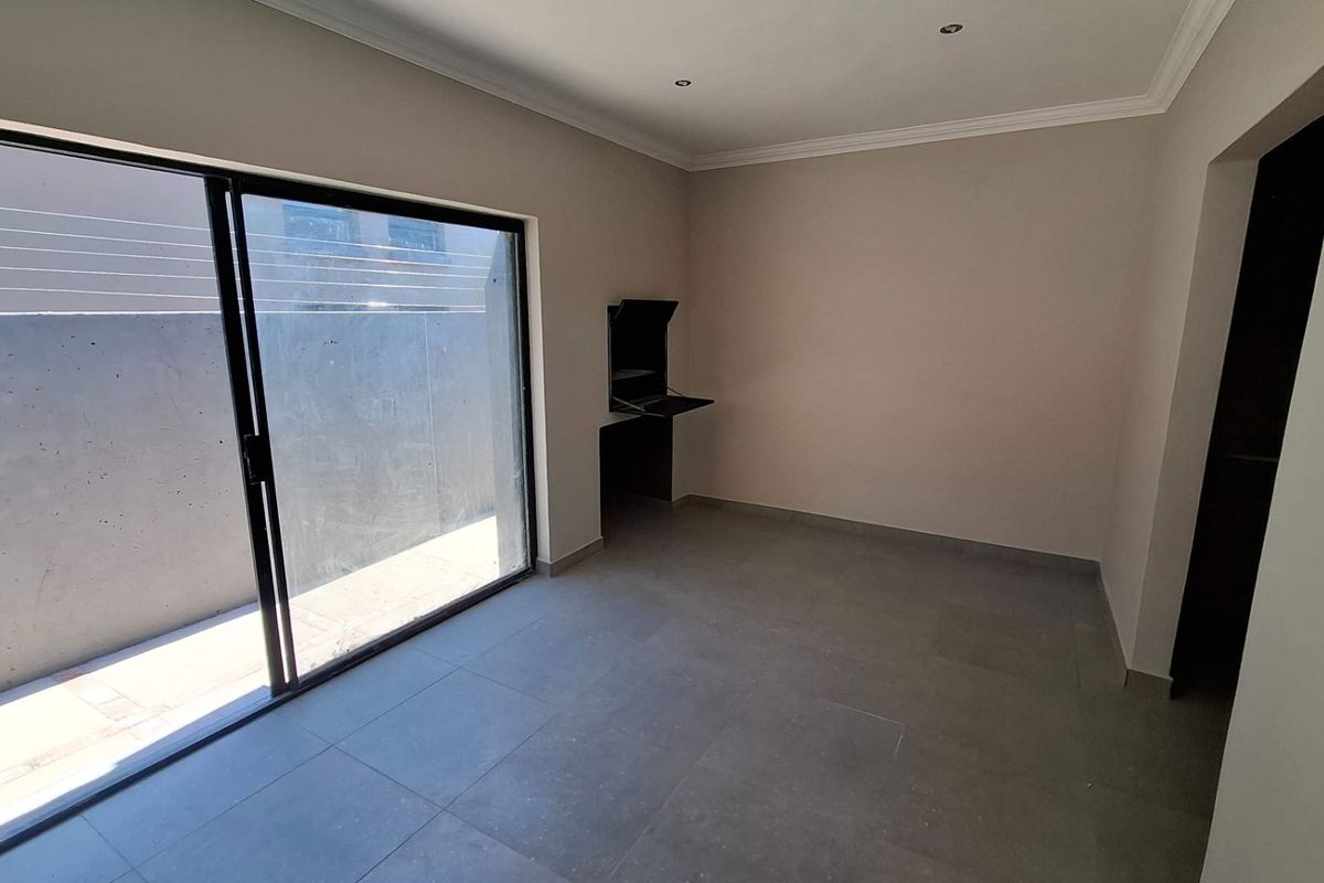 An empty, modern living area featuring large sliding glass doors, neutral tiled flooring, recessed lighting, and a convenient built-in wall desk.