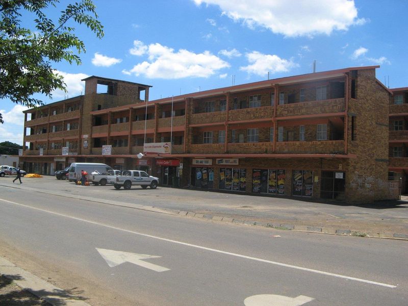A multi-level apartment building featuring a face brick facade with ground floor retail spaces and external access walkways.