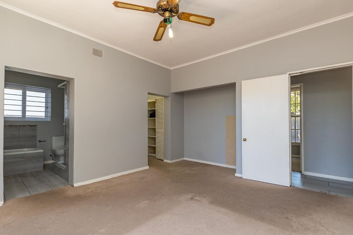 A spacious bedroom featuring neutral walls, a ceiling fan, built-in closet space, and an en-suite bathroom with tiled finishes.