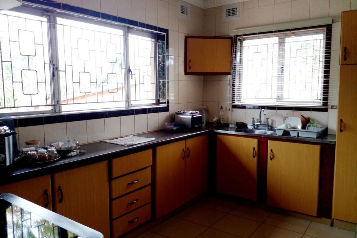 A functional kitchen featuring wood-look laminate cabinetry, dark countertops, tiled walls, and large windows with security bars, offering a dated but well-maintained workspace.