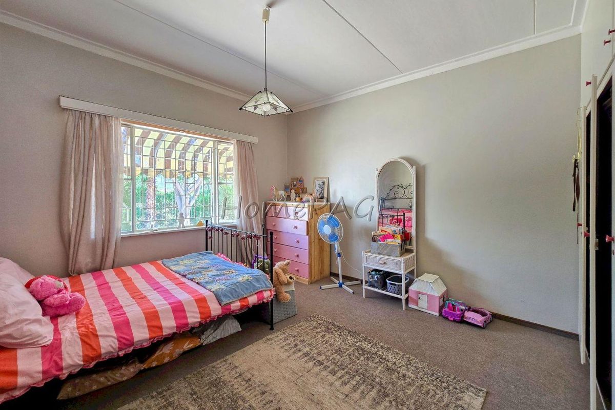 A bedroom featuring carpeted flooring, a large window with security bars, and built-in wardrobe storage.