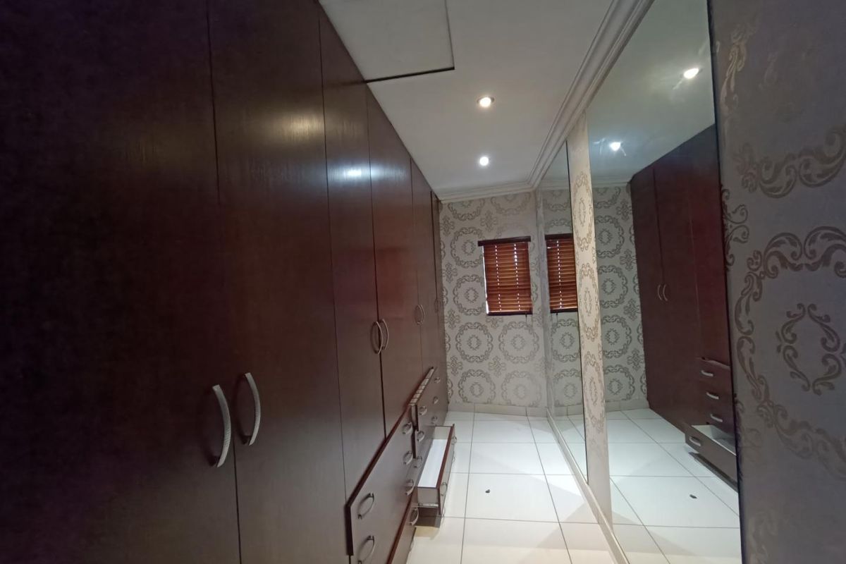 A well-appointed dressing room featuring extensive built-in dark wood cabinetry, full-length mirrored doors, tiled flooring, and recessed ceiling lighting.