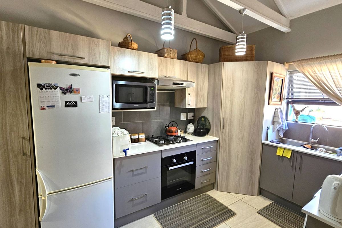 A functional kitchen featuring light wood-grain cabinetry, a built-in oven, gas hob, extractor fan, and a tiled backsplash with a stainless steel sink.