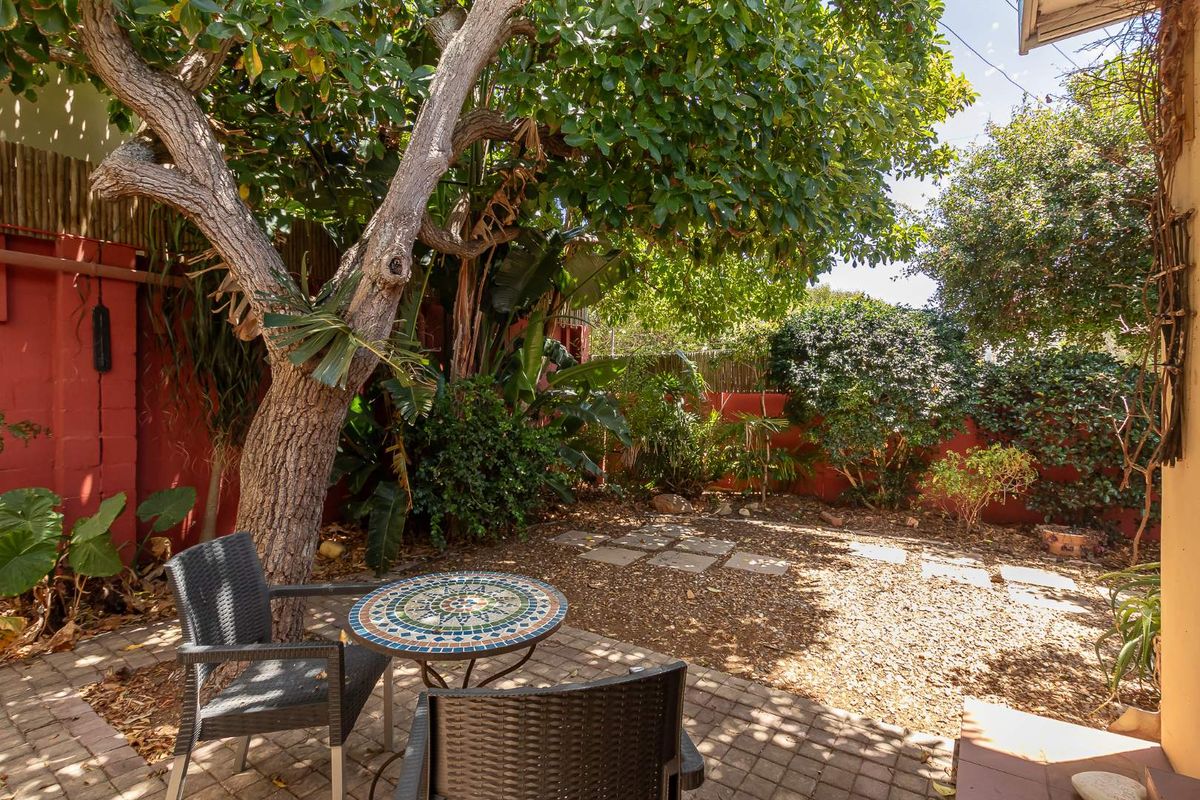 A private rear garden area featuring mature trees, established landscaping, a paved patio section, and enclosed by painted boundary walls.