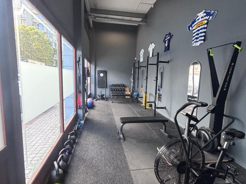 A functional gym space featuring durable rubber flooring, large street-facing windows, and exposed ceiling infrastructure, suitable for a retail or fitness studio setup.