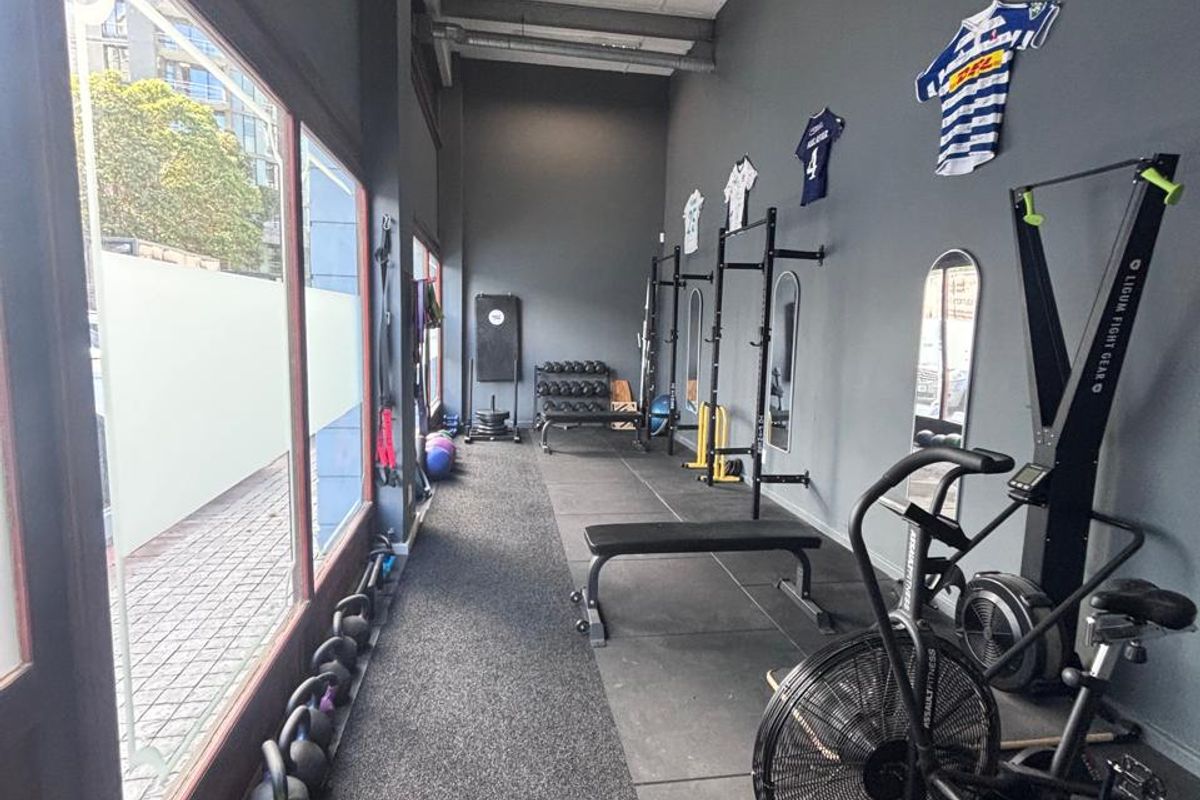 A functional gym space featuring durable rubber flooring, large street-facing windows, and exposed ceiling infrastructure, suitable for a retail or fitness studio setup.