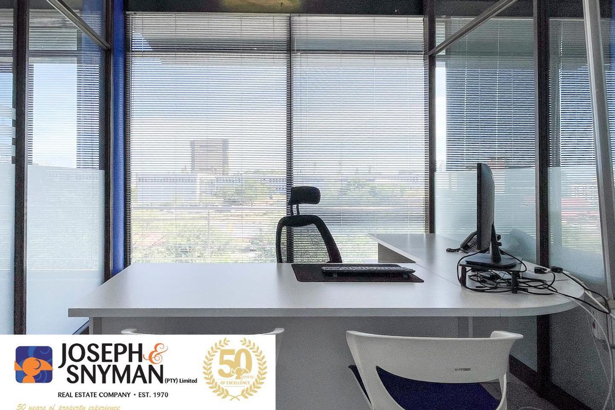 A professional office space featuring glass partitioning, built-in desk, and large windows with blinds, offering a bright and functional work environment.