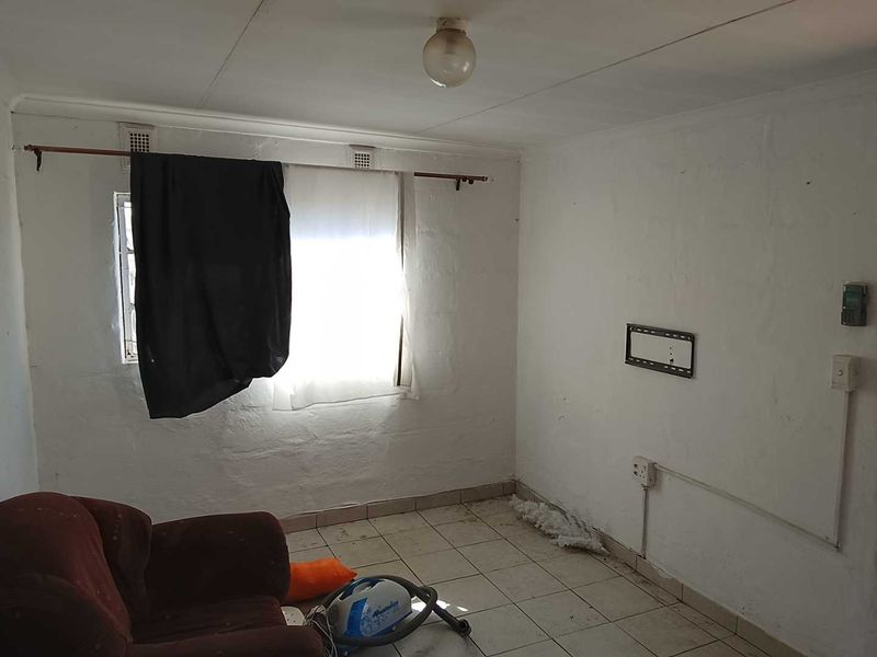 A basic, empty living area featuring tiled flooring and white walls, requiring cosmetic updates and maintenance to improve its overall condition.