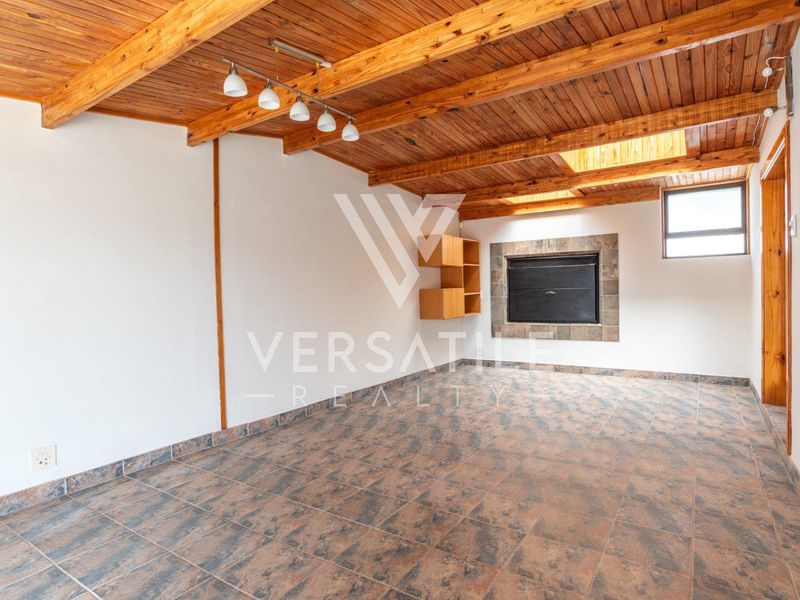 An empty living room featuring a rustic exposed timber beam ceiling, tiled flooring, a built-in fireplace, and a skylight for natural illumination.