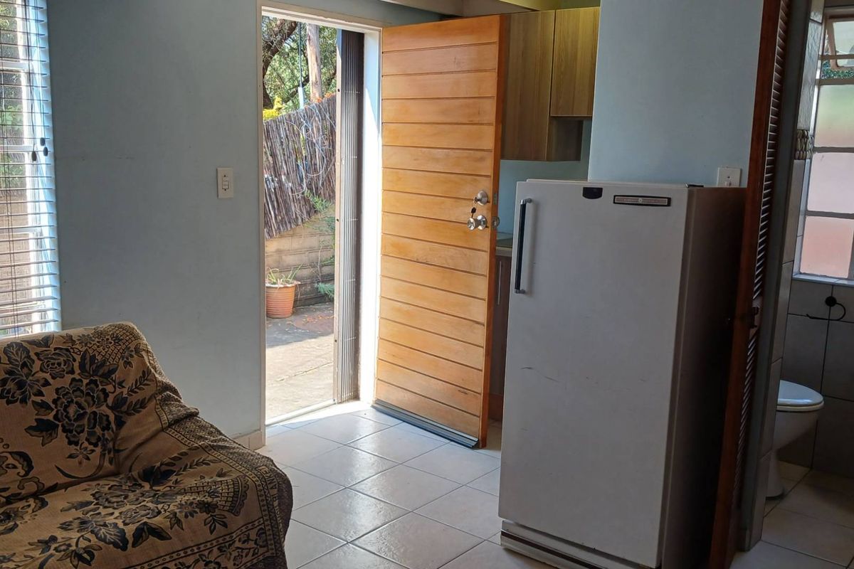 Open plan living area featuring tiled flooring, direct garden access through a timber door, and an adjacent bathroom area with a pedestal basin.