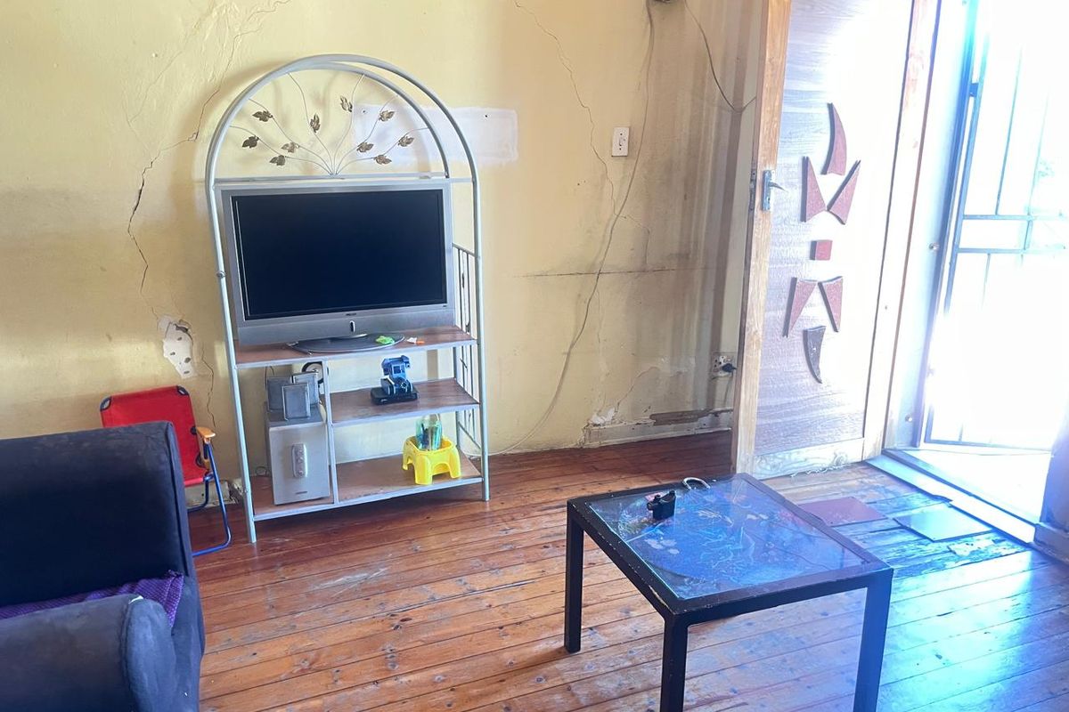 Living area featuring original timber flooring and an entrance door, currently showing significant wall cracking and plaster damage requiring maintenance.
