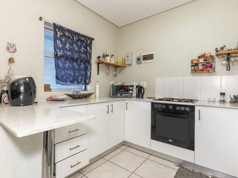 Compact kitchen featuring white cabinetry, stone-look countertops, built-in electric oven and hob, and tiled flooring.