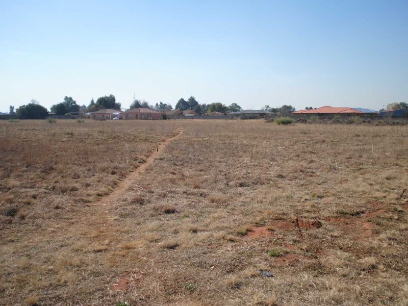 A wide-angle view of a vacant residential plot featuring dry grass and a perimeter boundary wall in a suburban setting.