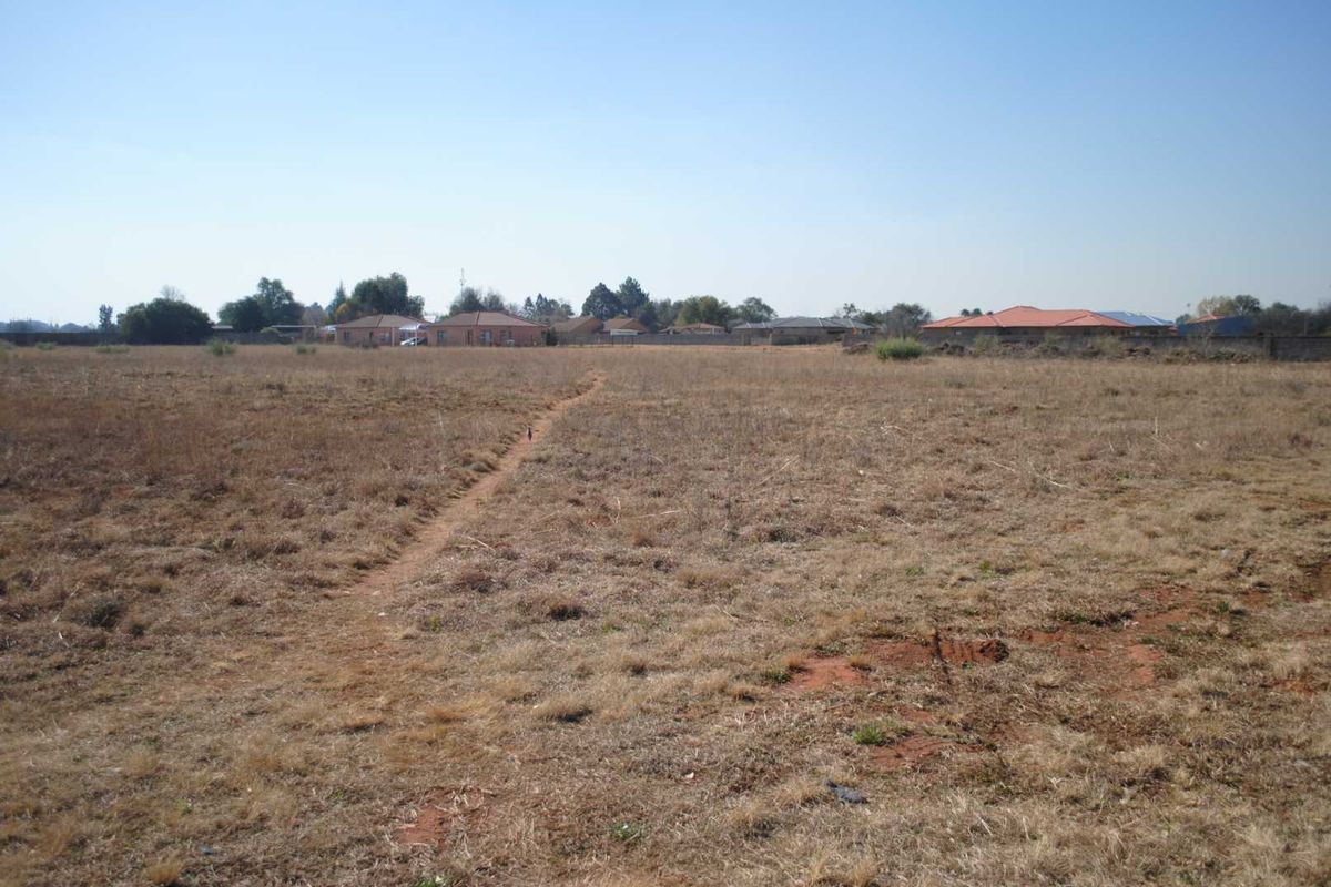 A wide-angle view of a vacant residential plot featuring dry grass and a perimeter boundary wall in a suburban setting.