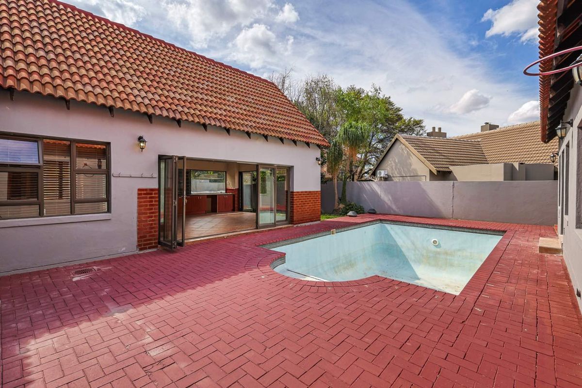 Rear exterior view featuring a paved patio area, a swimming pool, and large folding doors leading into the interior living space.