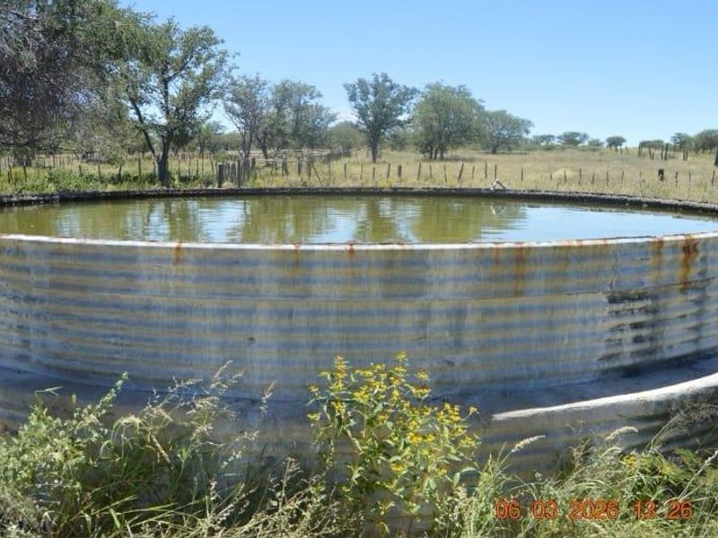 A large corrugated metal water reservoir tank situated on a concrete base, located in an open farm landscape.