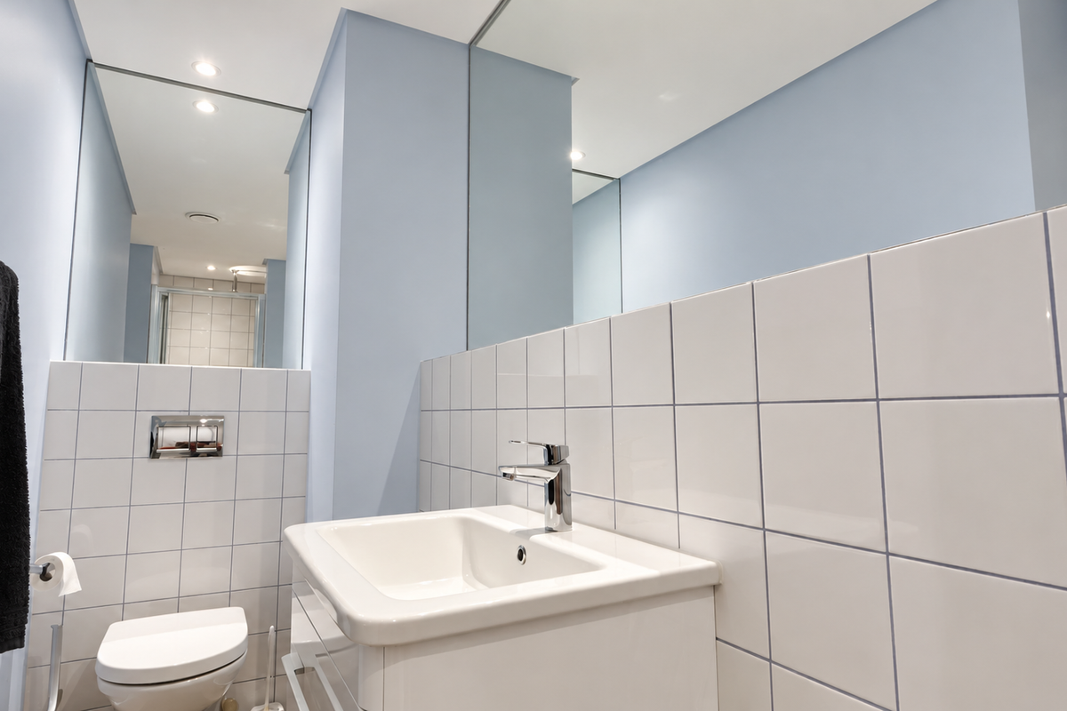 A clean and modern bathroom featuring a wall-mounted toilet, vanity basin with chrome mixer tap, and large wall mirrors.