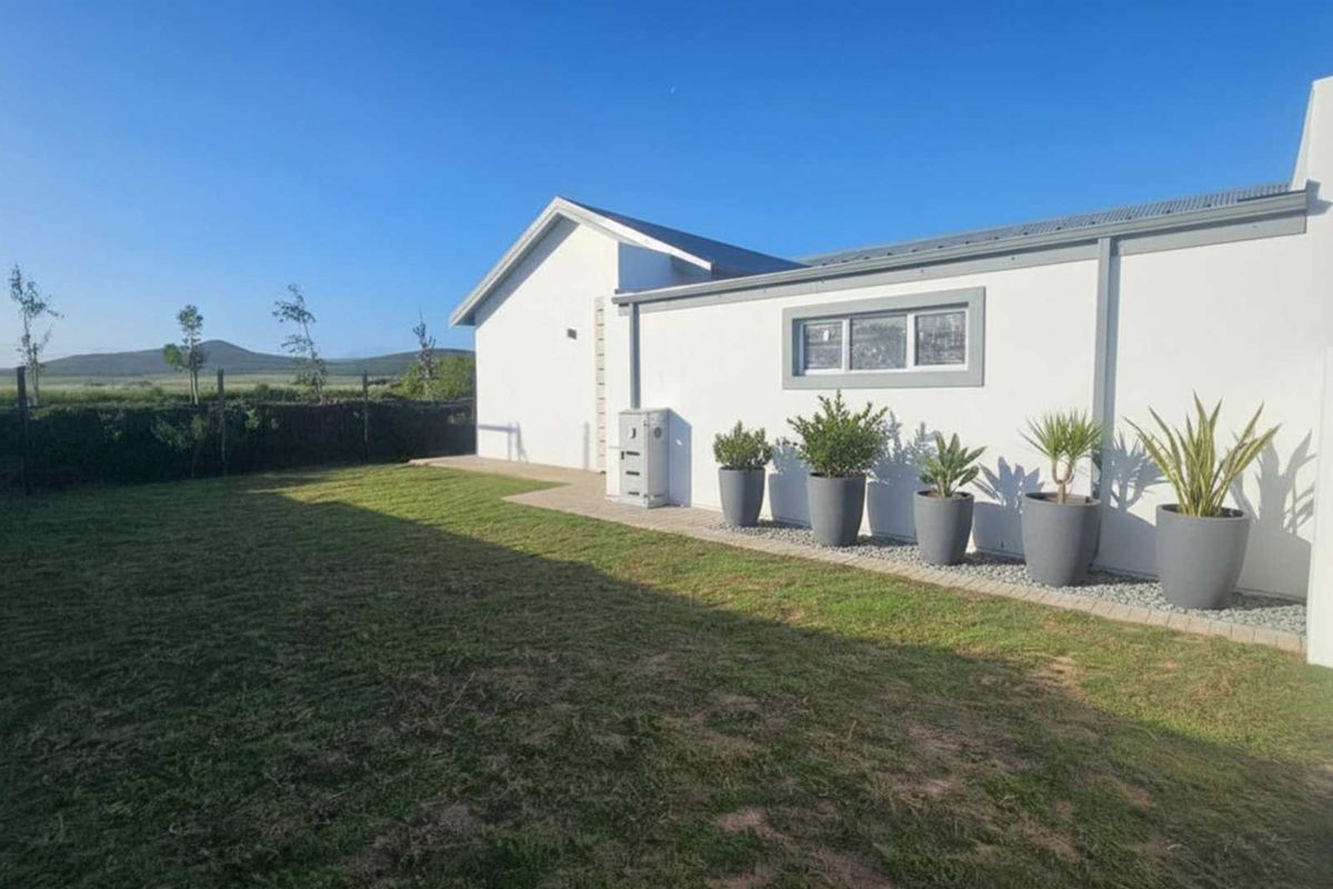 A well-maintained rear garden featuring a manicured lawn, paved border, and a clean white exterior wall of the house.