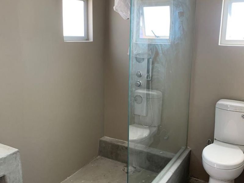 An unfinished bathroom featuring a glass shower screen, toilet, and concrete flooring, requiring final finishes and fixtures to complete the space.
