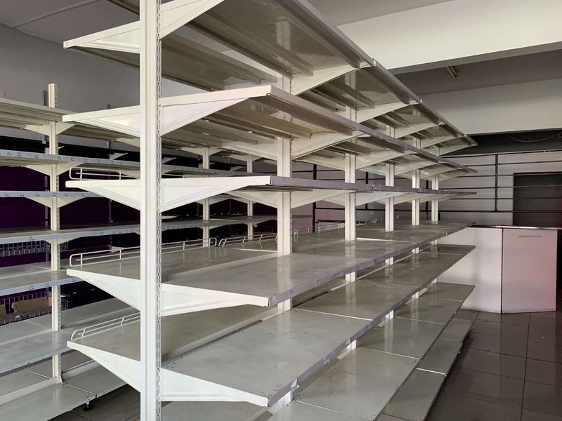 Empty retail space featuring modular metal shelving units, slatwall display panels, and tiled flooring, suitable for various commercial or retail business applications.