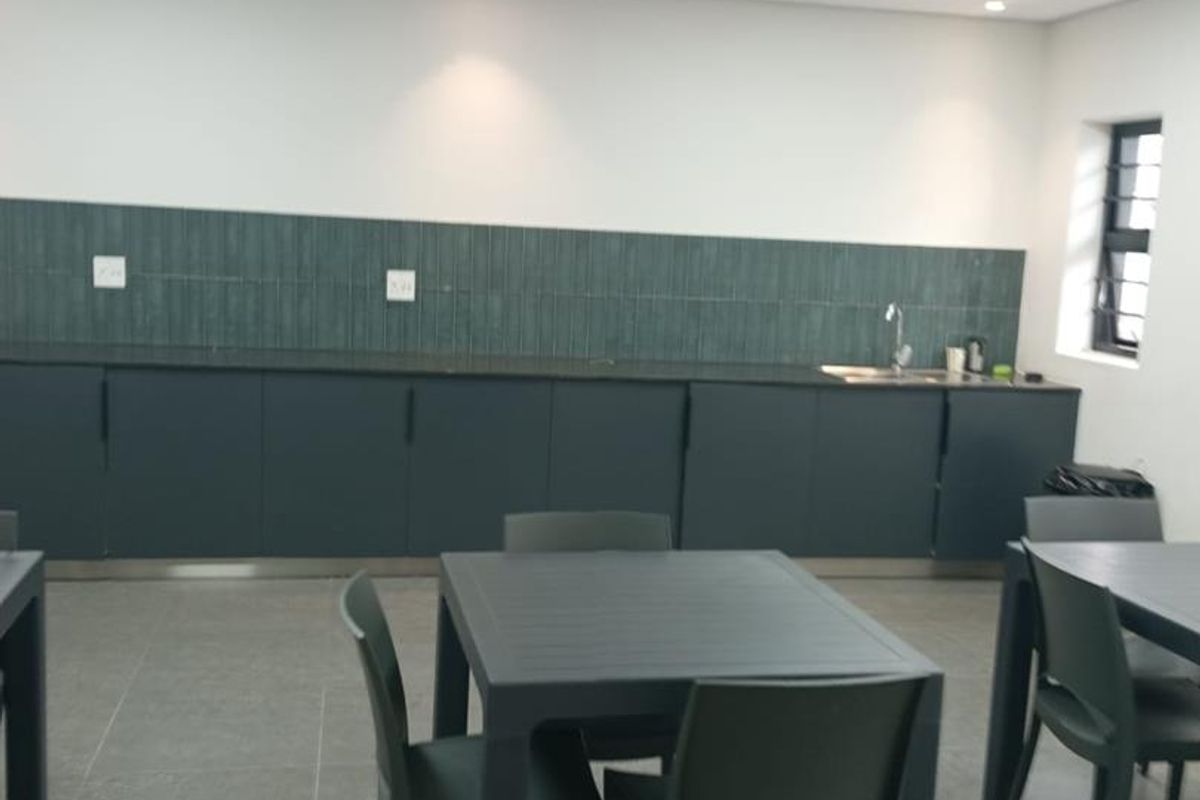 A clean, modern industrial kitchen area featuring dark cabinetry, a tiled backsplash, integrated sink, and recessed lighting in a drop ceiling.