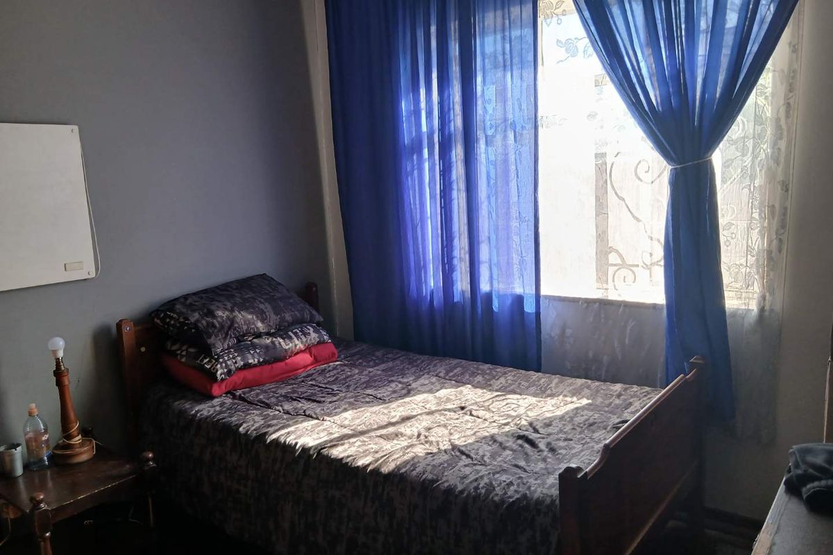 A compact bedroom featuring a window with blue curtains and dark grey painted walls.