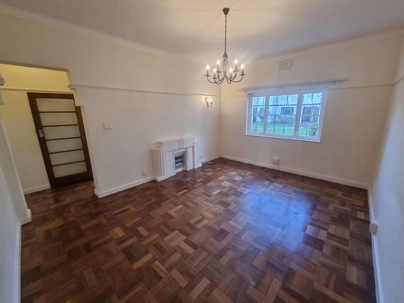 Spacious living room featuring original parquet flooring, an art deco fireplace, and classic architectural details including coved cornicing and picture rails.