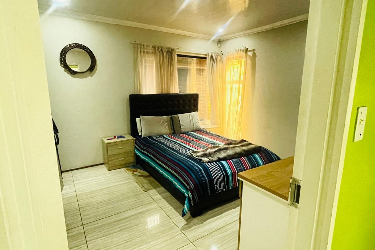 A bedroom featuring tiled flooring, neutral walls, and a window with sheer curtains, providing a functional and well-lit sleeping space.