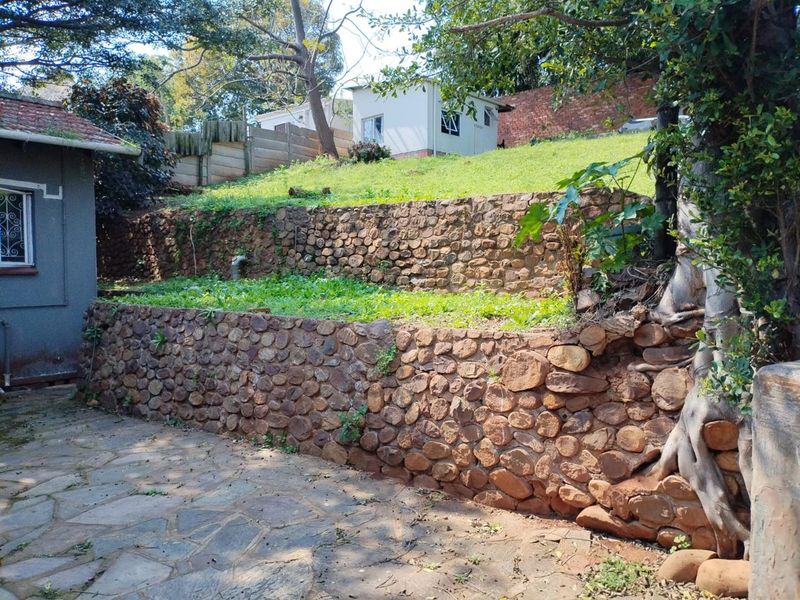 Rear garden area featuring tiered stone retaining walls, a paved patio section, and an elevated grassed yard.