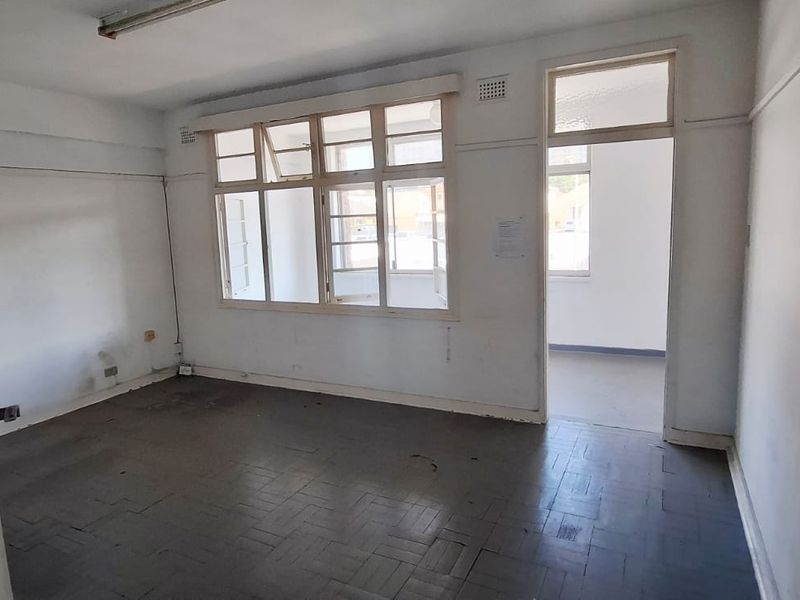 An empty office space featuring original parquet flooring, timber-framed windows, and a functional layout suitable for a professional workspace.