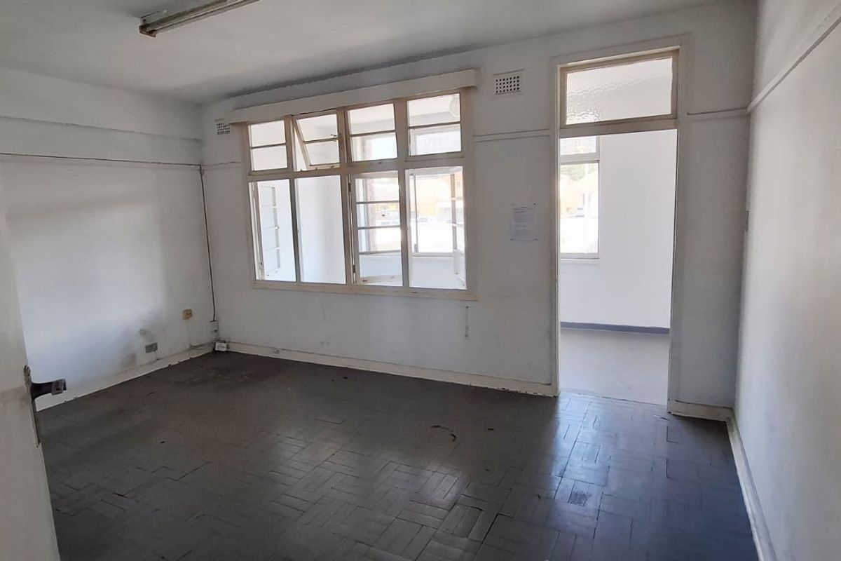 An empty office space featuring original parquet flooring, timber-framed windows, and a functional layout suitable for a professional workspace.