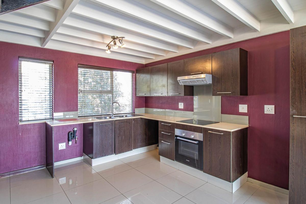 A clean, functional kitchen featuring dark wood cabinetry, built-in oven and hob, tiled flooring, and a distinctive exposed beam ceiling.