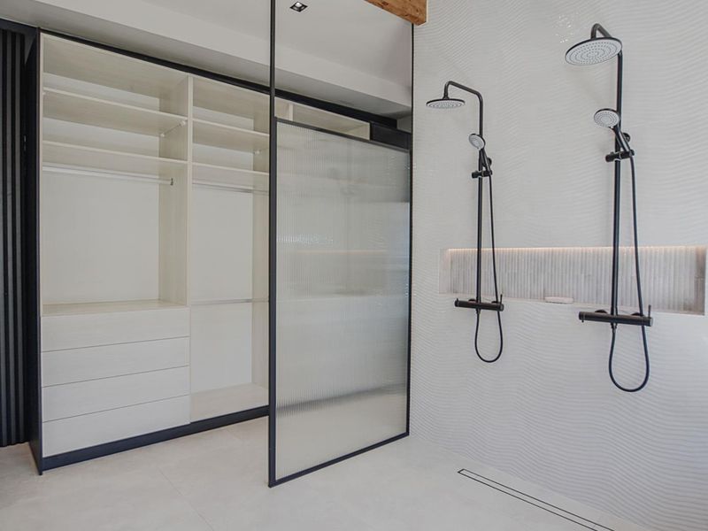 Modern bathroom featuring a dual shower setup with matte black fixtures, a recessed niche, fluted glass partition, and integrated wardrobe storage.
