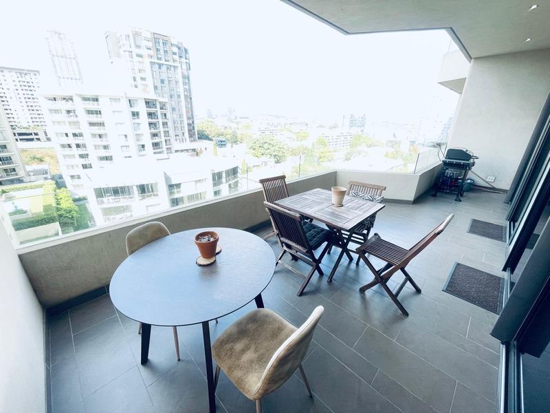 Spacious covered balcony featuring modern tiled flooring, a glass balustrade, and expansive city views, perfect for outdoor dining and relaxation.