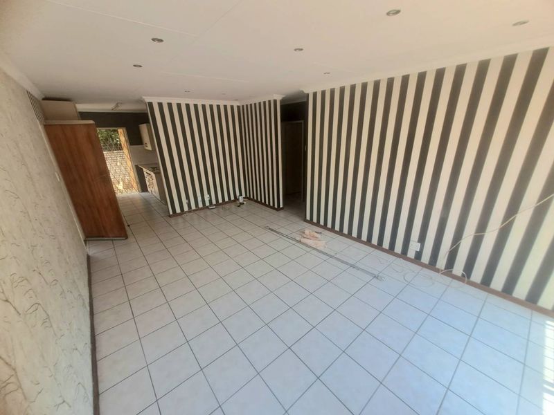 An empty open-plan living and kitchen area featuring tiled flooring, recessed lighting, and distinctive striped wallpaper throughout the space.